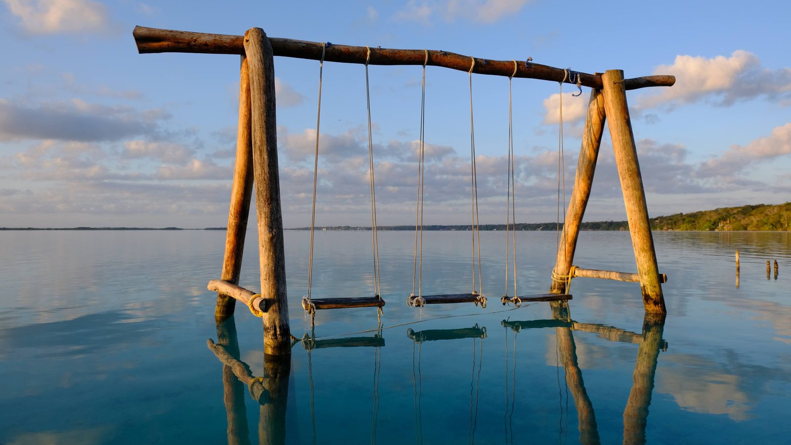 Columpios de madera colgando sobre agua turquesa cristalina en un muelle de la Laguna de Bacalar