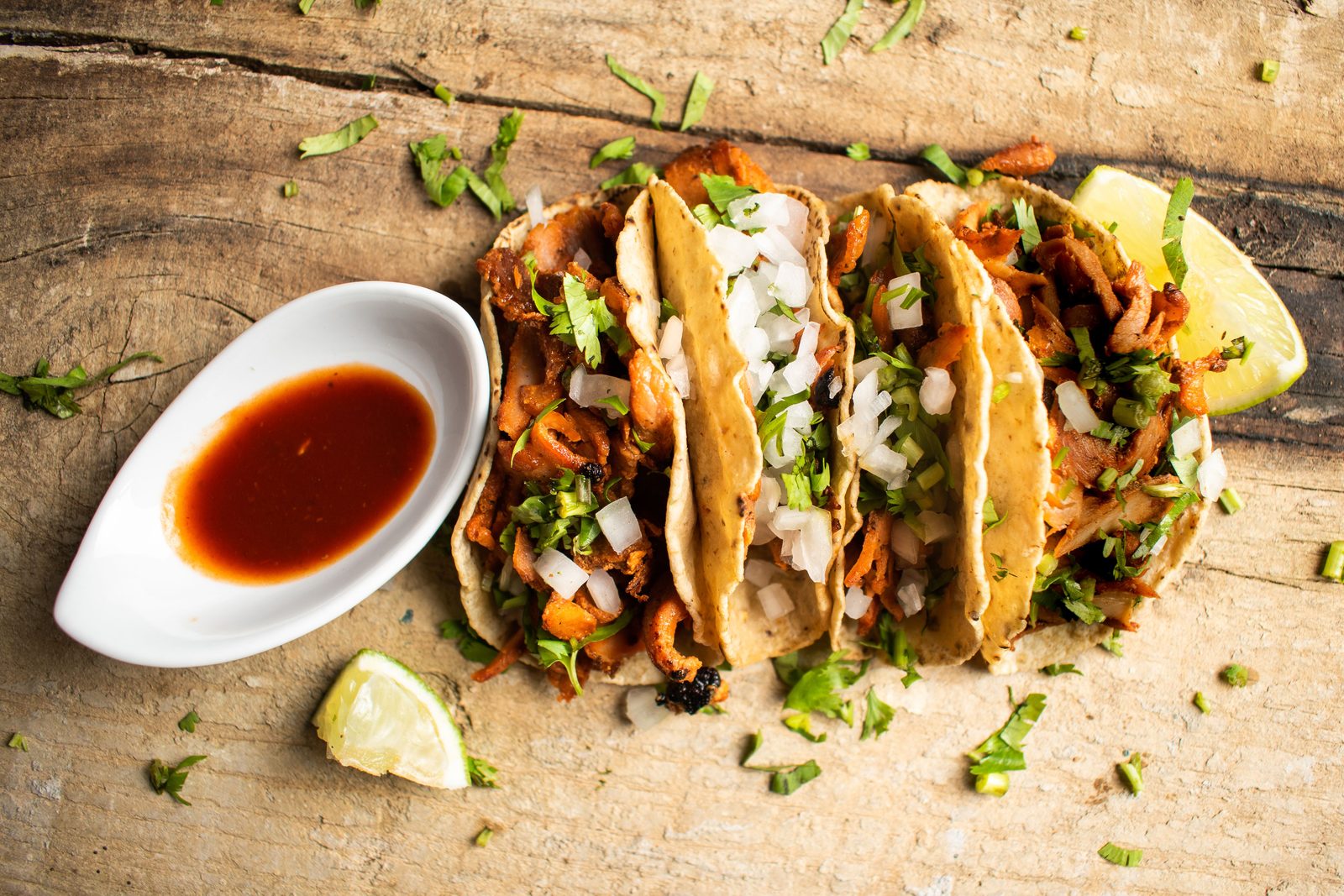 Three tacos al pastor topped with cilantro, onion and lime on a Tulum table