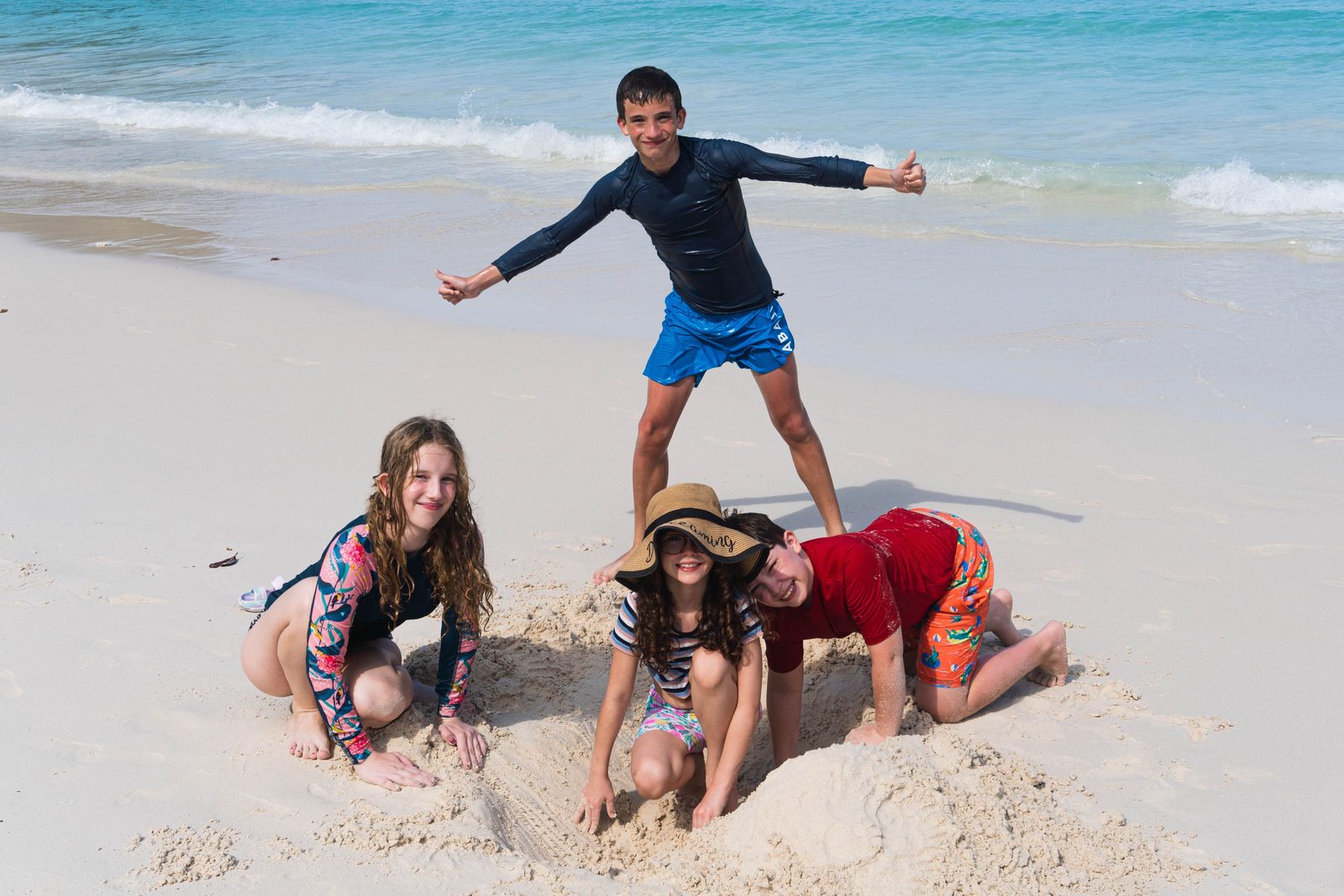 Children playing on a white-sand beach beside turquoise Caribbean water in Tulum