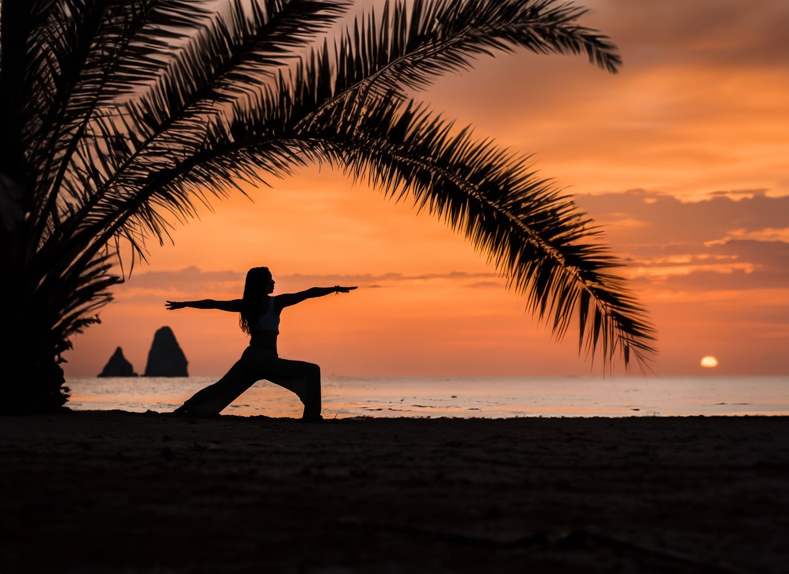 Woman practicing yoga under palm trees at sunset in Tulum